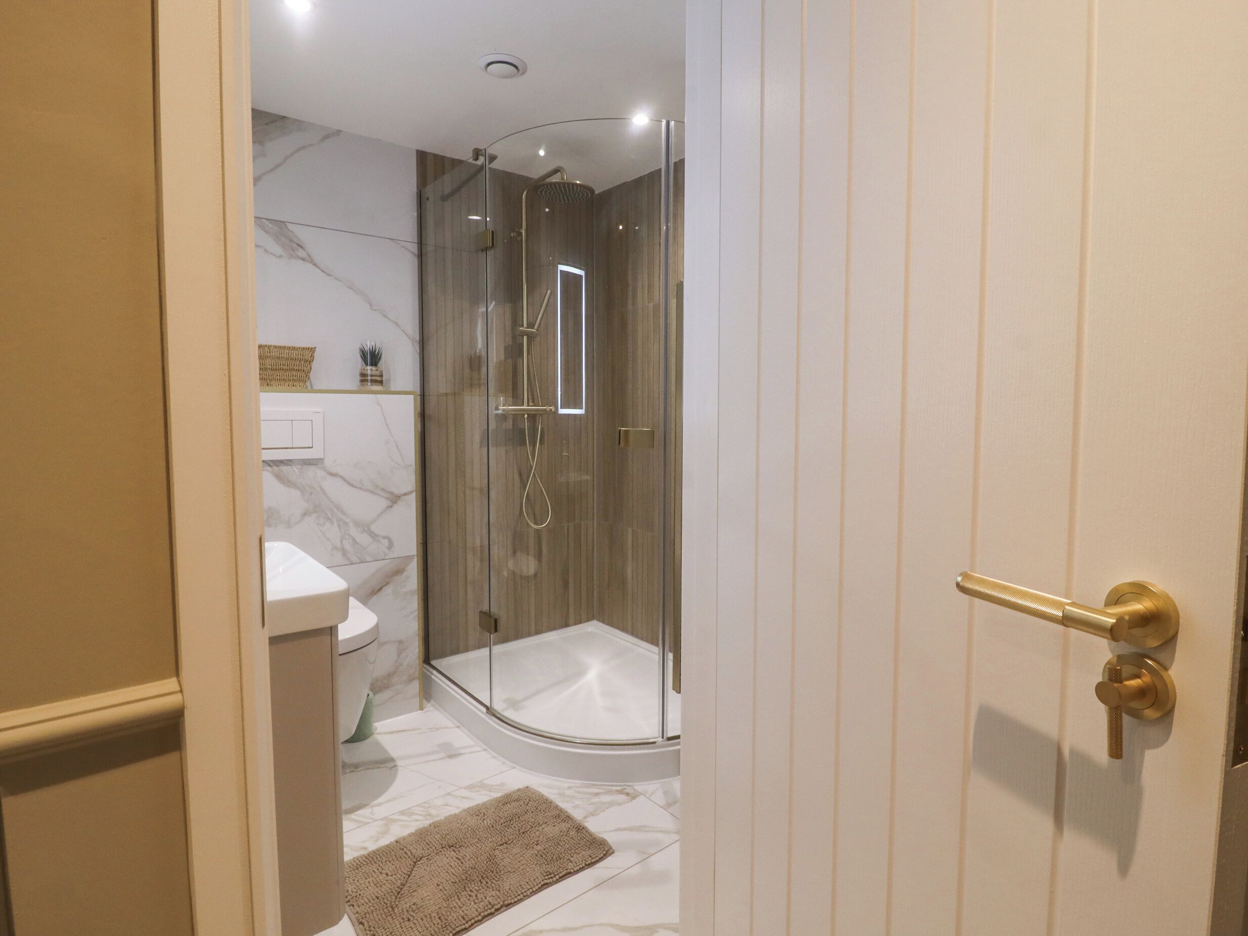 Une salle de bain moderne avec une douche à parois de verre, des toilettes blanches et un sol carrelé en marbre.