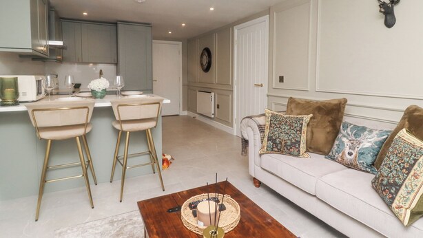 A modern kitchen with a bar area, a white sofa with decorative pillows, and a wall-mounted deer head. - Eden Cottage (Keighley)