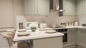 A modern kitchen with a central island, bar stools, a built-in oven, and stainless steel appliances. - Eden Cottage (Keighley)