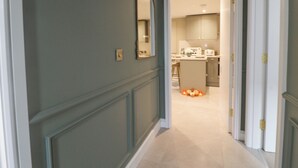 A hallway with a mirror, a light switch, and a door leading to a kitchen area. - Eden Cottage (Keighley)
