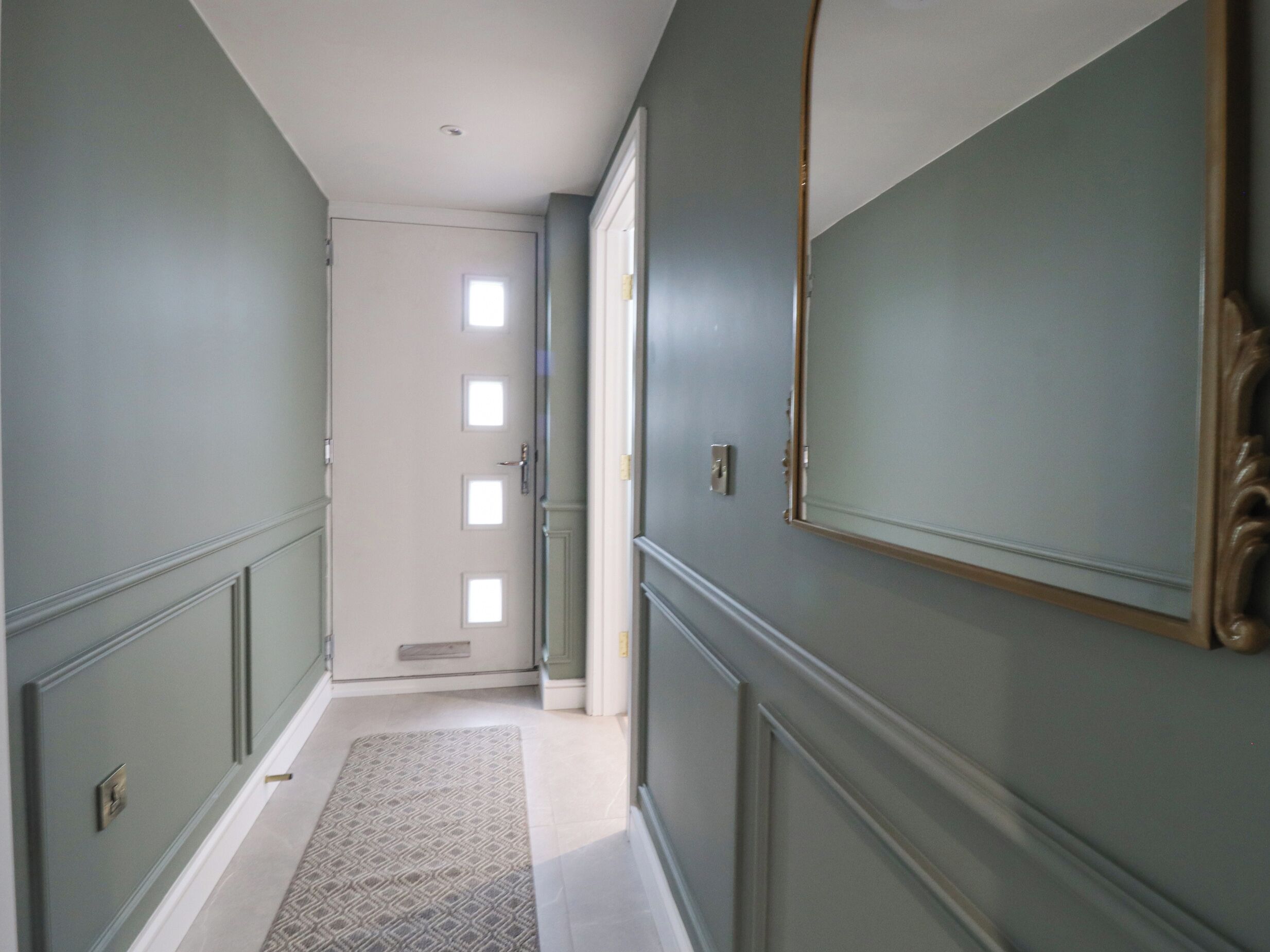 A hallway with a door at the end, a patterned rug, and a mirror on the wall.