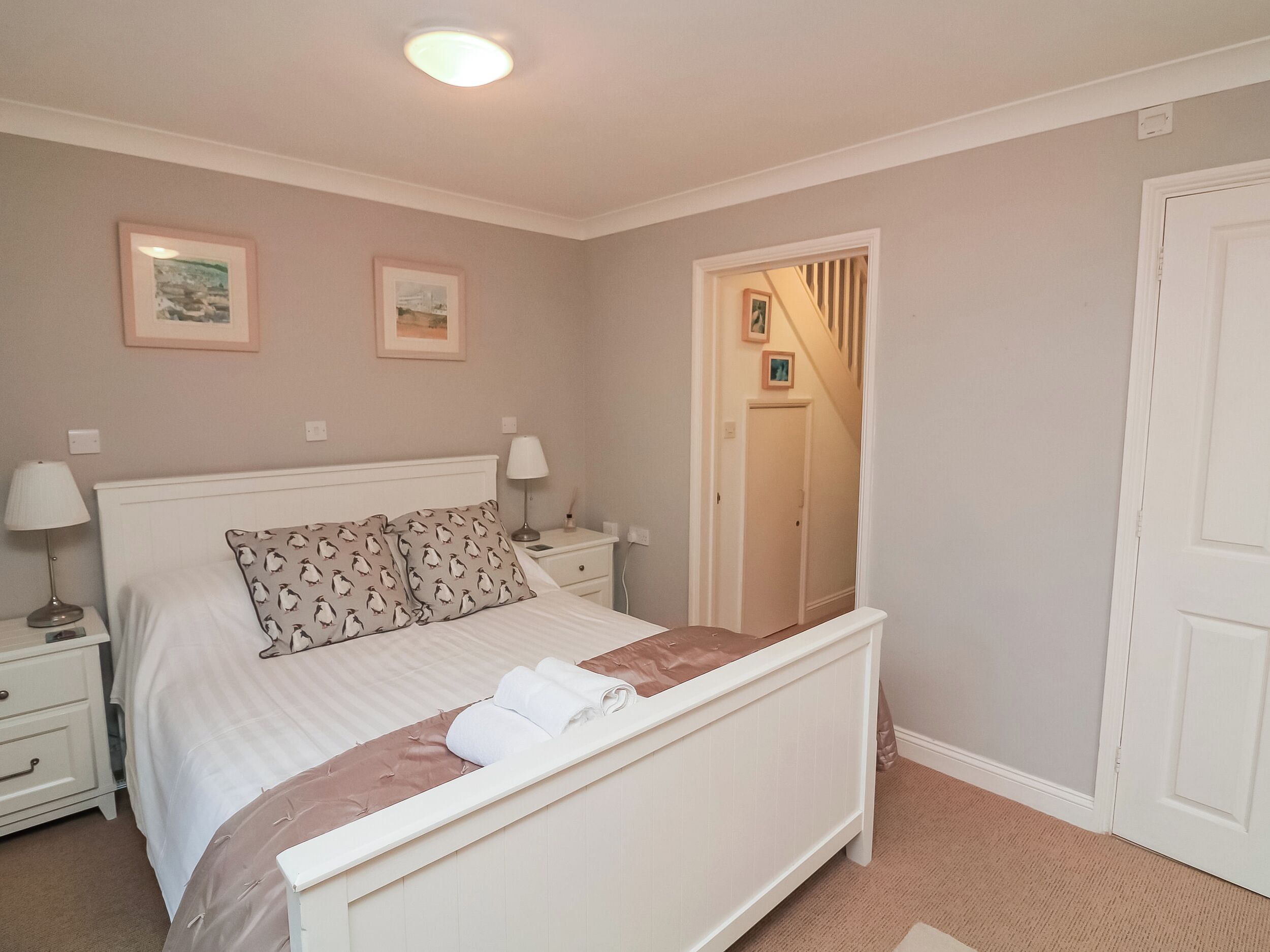 A bedroom with a bed, bedside tables, a nightstand, a door, and a framed picture on the wall.