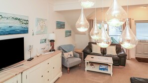 A living room with a flat-screen TV, a wooden cabinet, a grey armchair, a brown leather sofa, and a coffee table. - 22 Bolt Head (Salcombe)