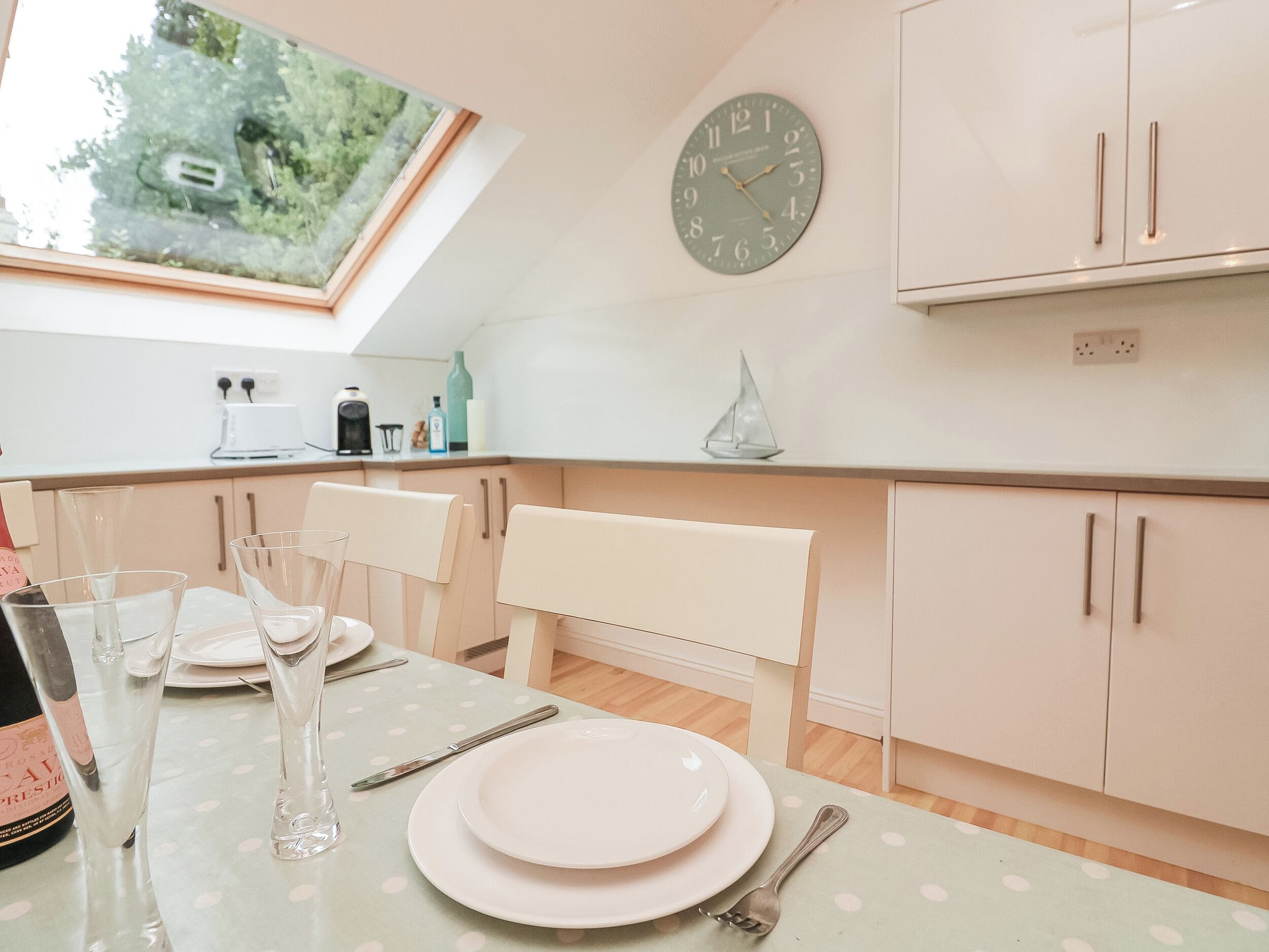 A modern kitchen with a dining area, featuring a clock, cabinets, and a view through a skylight.