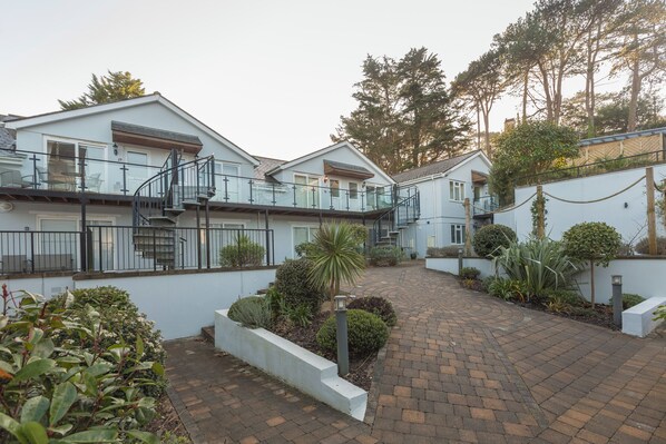 A residential building with a central courtyard, featuring a brick pathway, a glass balustrade, and various plants. - 22 Bolt Head (Salcombe)