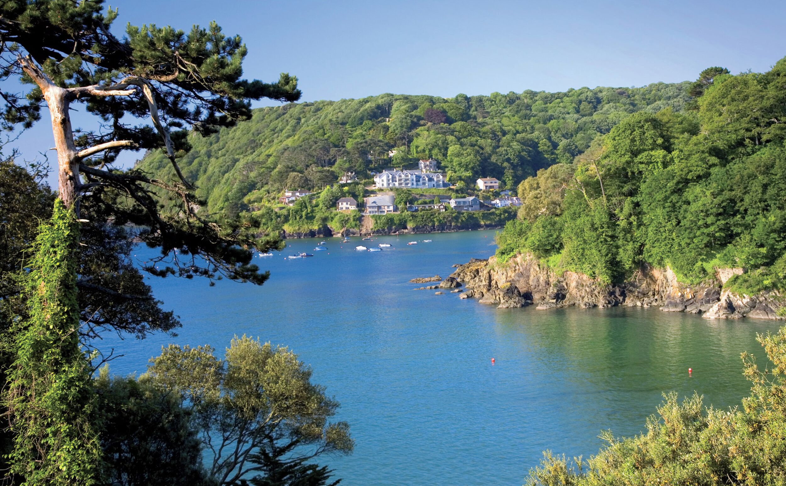 A coastal area with a large body of water, surrounded by lush green hills and a few buildings.