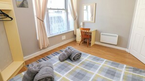 A bedroom with a bed, a desk, a chair, a radiator, and a window with curtains. - The Hilton Retreat (Tenby)