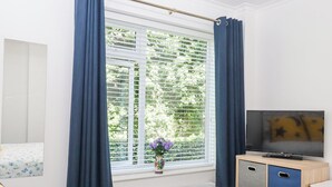 Une chambre à coucher avec un lit, une télévision, une fenêtre avec des rideaux et un vase rempli de fleurs.