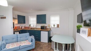 Un espacio habitable compacto con kitchenette, un sofá azul, una mesita redonda y un televisor montado en la pared.