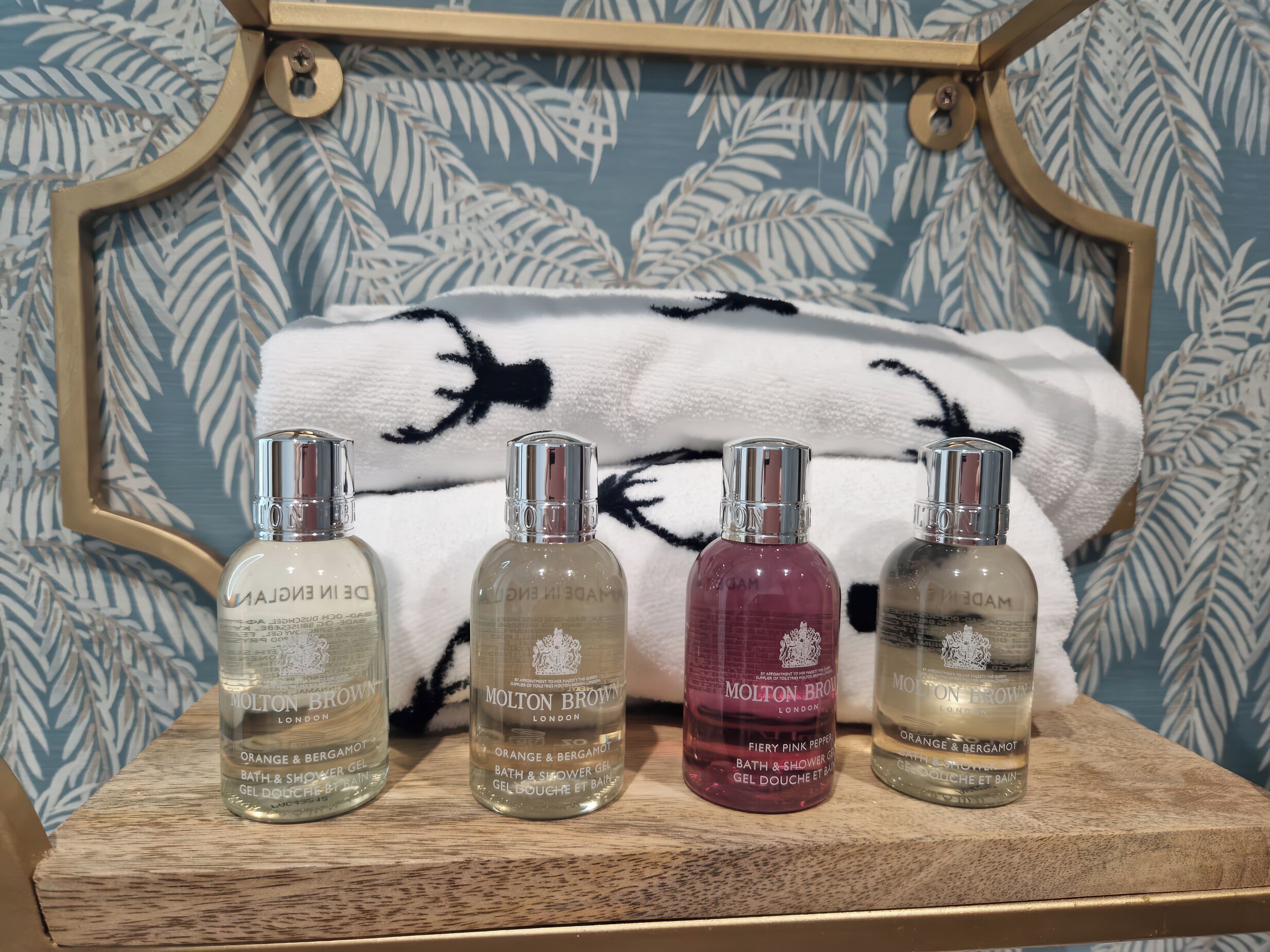 Cuatro botellas de gel de baño y ducha Molton Brown sobre un estante de madera.