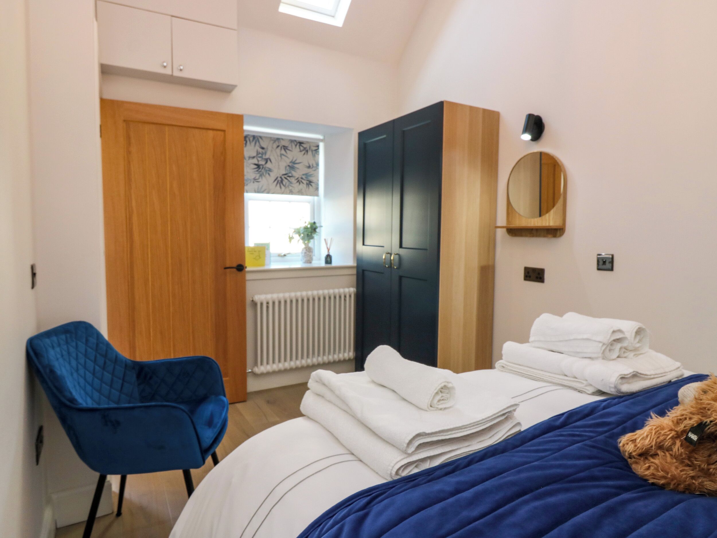 Ein Schlafzimmer mit einem Bett, einem blauen Sessel, einem Kleiderschrank und einem Fenster mit Blick nach draußen.