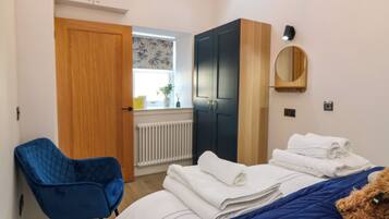 Ein Schlafzimmer mit einem Bett, einem blauen Sessel, einem Kleiderschrank und einem Fenster mit Blick nach draußen.