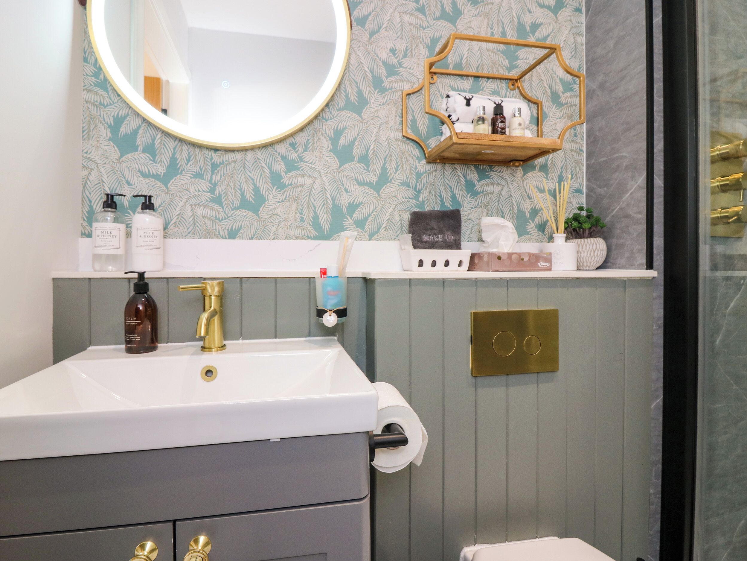 A bathroom with a white sink, gold faucet, and a mirror. There is a towel rack with a towel and a small shelf with toiletries.