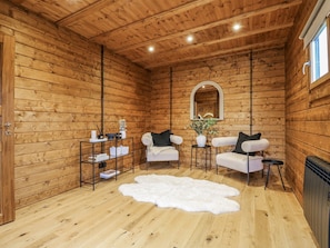 Ein gemütliches Blockhaus-Interieur mit Holzwänden, einem weißen Fellteppich, zwei weißen Sesseln, einem kleinen Tisch mit einer Vase und einem Spiegel an der Wand.