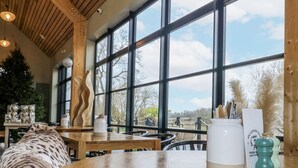 A cozy seating area with a round wooden table, a decorative vase, and a view through large windows. - Badger's Burrow (Oakham)