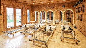 A wooden interior with multiple massage tables arranged in rows, a visible outdoor area through glass doors, and a wall-mounted mirror. - Badger's Burrow (Oakham)