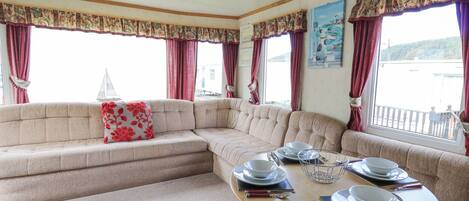 A cozy seating area with a sofa and a dining table set for two, featuring a view of the water outside.