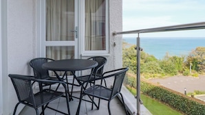 A balcony with a table and chairs, a view of the sea, and a parking area. - Godrevy View (St Ives)
