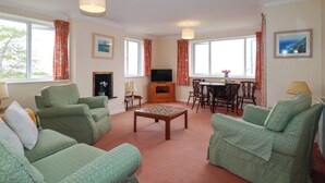 A living room with green upholstered sofas, a coffee table, a TV, and a dining area with a table and chairs. - Godrevy View (St Ives)