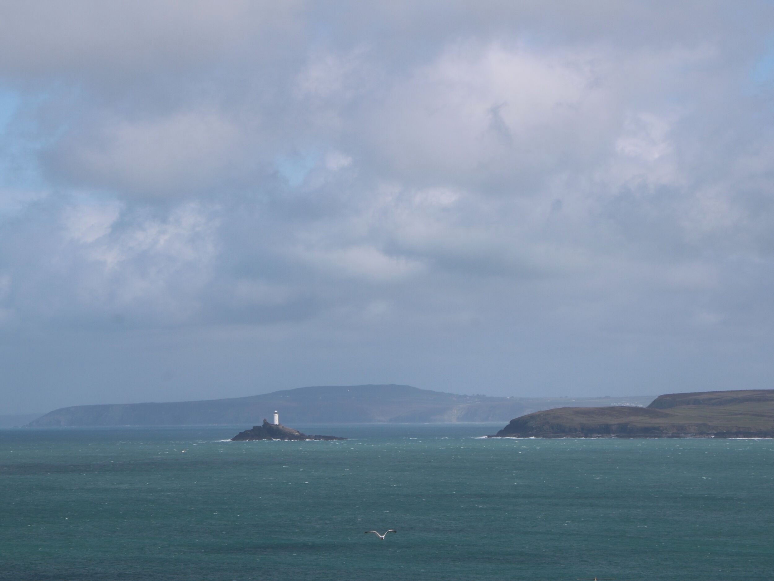 A lighthouse on a small island surrounded by calm sea and distant hills.