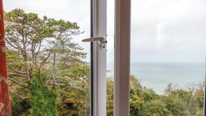 A view through a window with a door, overlooking a coastal landscape with trees and a road. - Godrevy View (St Ives)