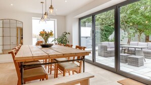 A spacious dining area with a long wooden table and benches, a large sliding glass door leading to an outdoor patio with wicker furniture and a view of greenery. - The Old Chapel (Gainsborough)