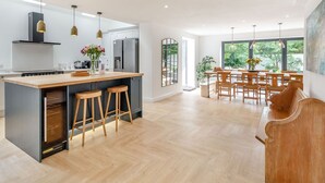 A modern kitchen with a central island, bar stools, and a dining area with wooden chairs and a large window. - The Old Chapel (Gainsborough)