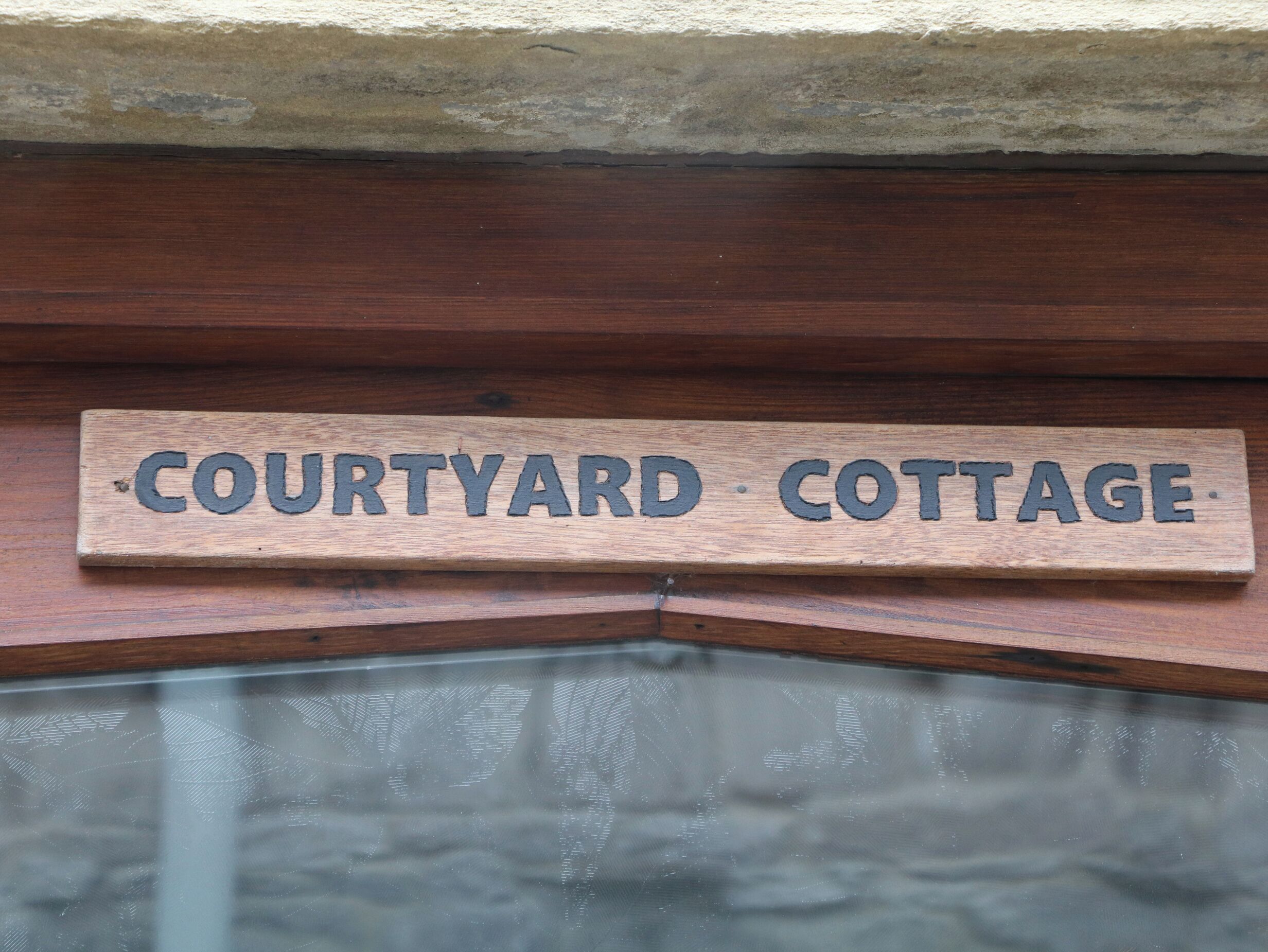 A wooden sign with the text "Courtyard Cottage" indicating the name of a property.