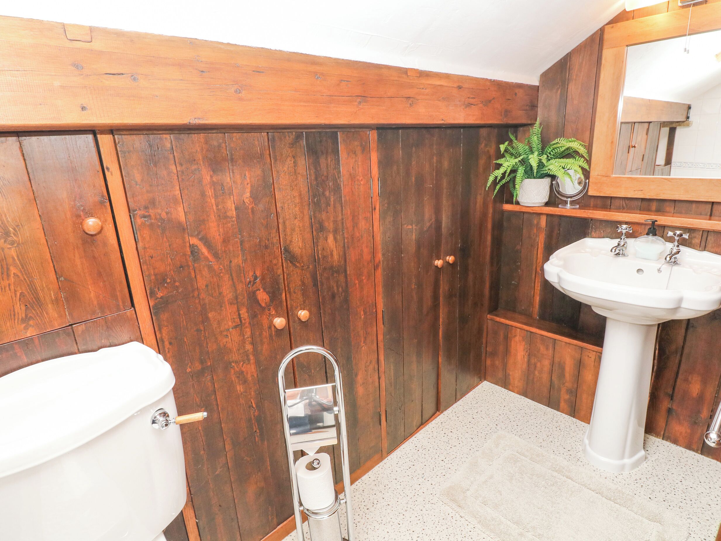 A bathroom with wooden walls, a white sink, and a toilet.