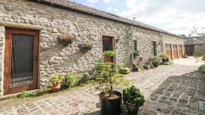 Un bâtiment en pierre avec une cour pavée, des plantes en pot et un petit arbre.