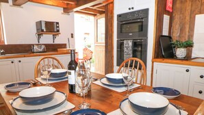 Une table à manger dressée avec de l’argenterie bleue, des verres à vin et des couverts, dans une cuisine dotée de meubles en bois et d’un four Bosch.