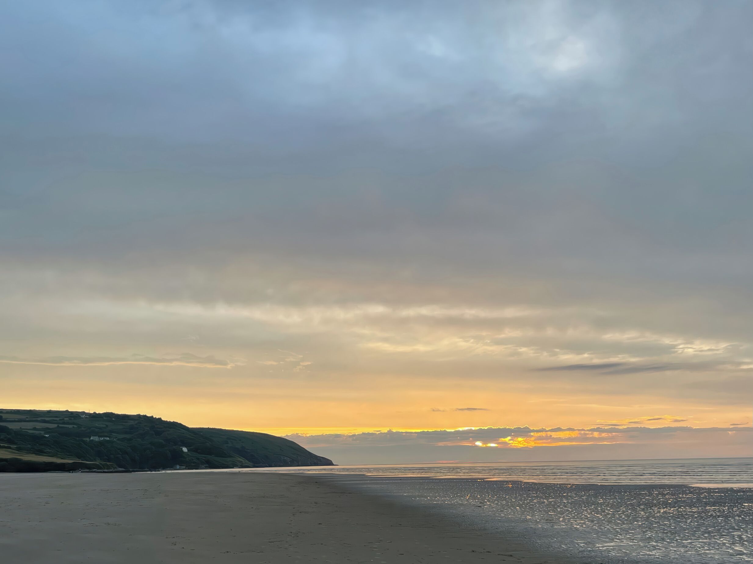 A beach with a wide sandy shore and a hilly landscape in the background.