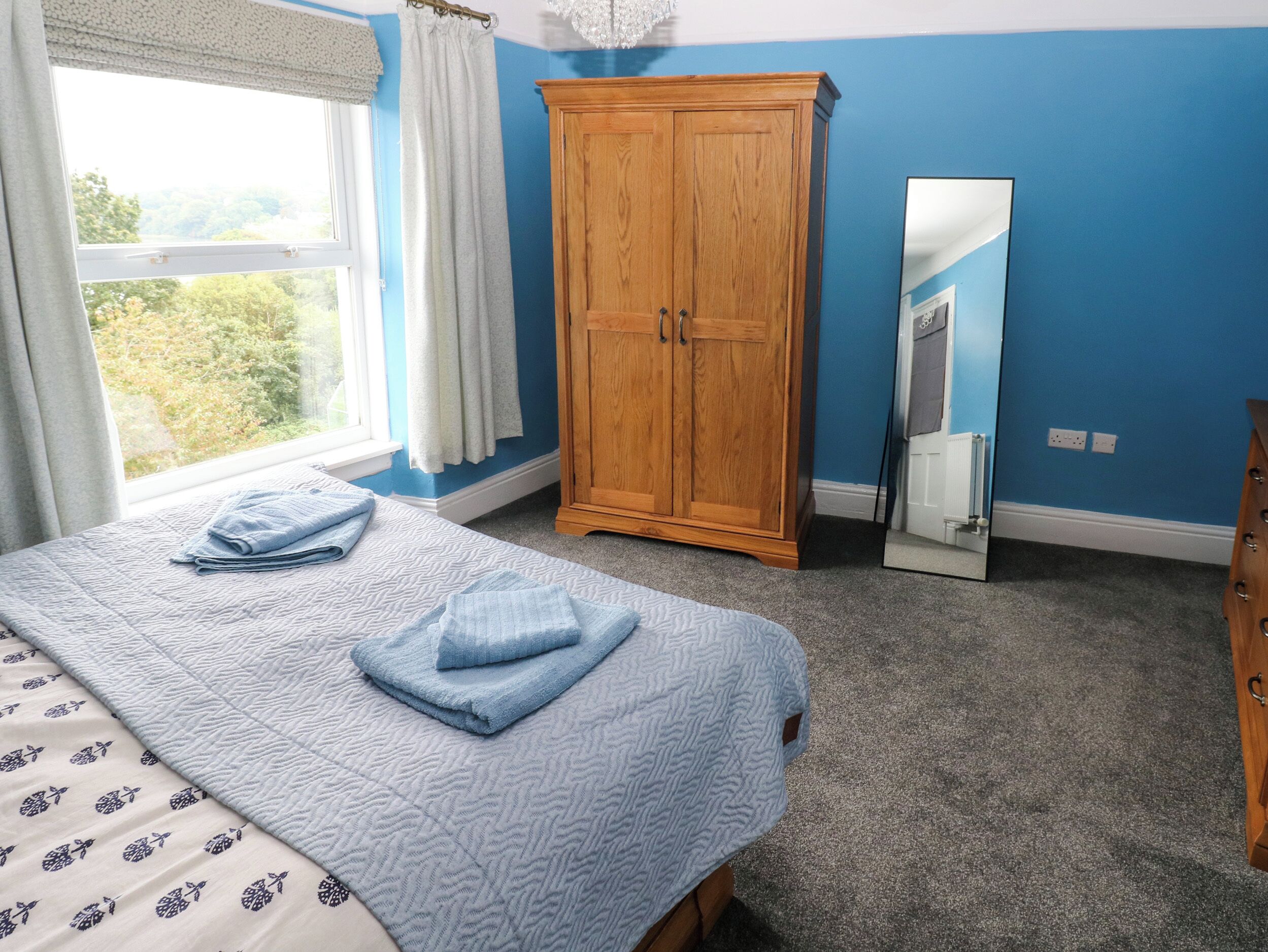 A bedroom with a bed, a wardrobe, a mirror, and a window with curtains.