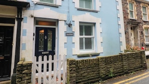 A two-story house with a blue and white exterior, a stone wall, and a white picket fence. - Rushfield (Cardigan)
