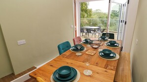 A dining area with a wooden table set for four, surrounded by chairs, and a view of the outdoors through a glass door. - Rushfield (Cardigan)