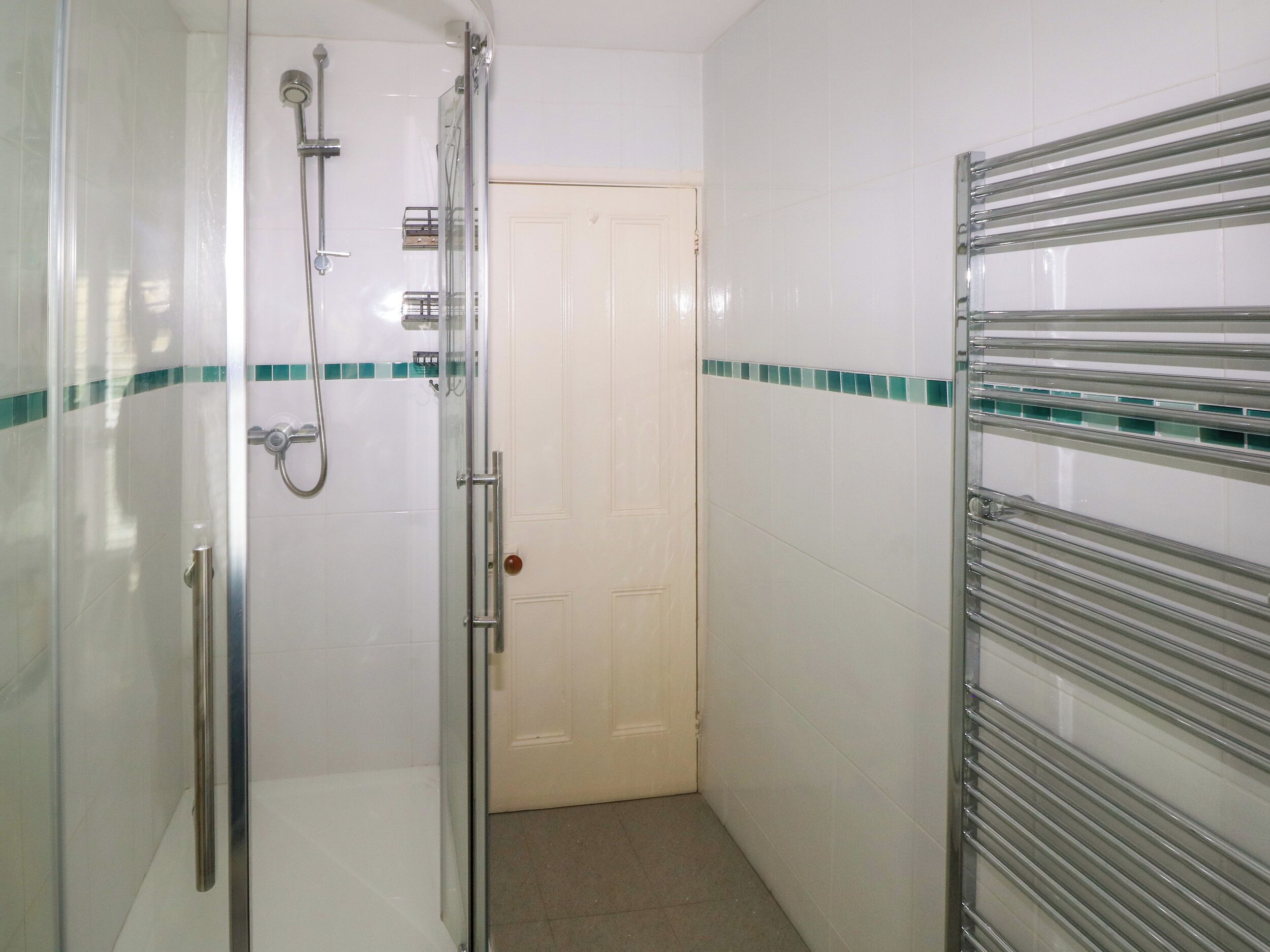 A bathroom with a glass shower enclosure, a white door, and a towel rack.