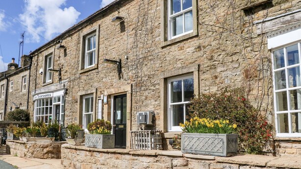 A stone building with multiple windows and doors, a sign for 'The Tea Room', and flower boxes on the front. - Keartons - Buttertubs (Richmond)