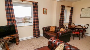 A living room with a leather sofa, a television on a wooden stand, plaid curtains, a dining table with chairs, and a framed picture on the wall. - Keartons - Buttertubs (Richmond)