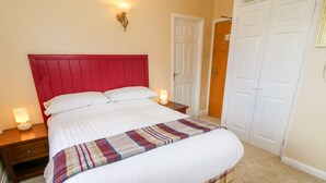 A bedroom with a red headboard, white bedding, a colorful blanket, bedside lamps, and a carpeted floor. - Keartons - Buttertubs (Richmond)