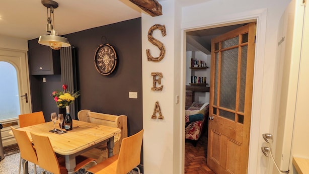 Zona pranzo con tavolo e sedie in legno, orologio a parete e la scritta decorativa 'SEA'.