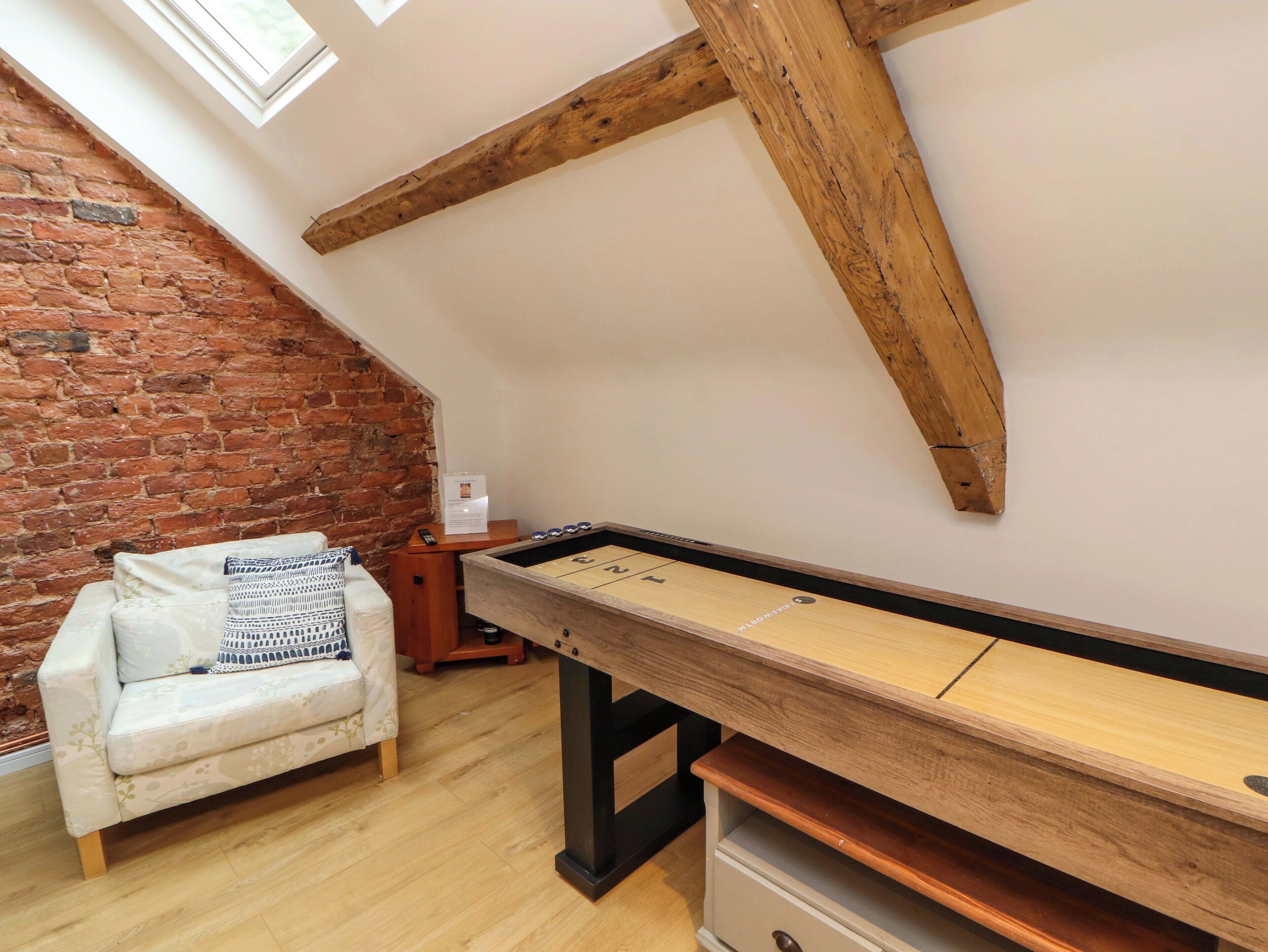 A room with a sloped ceiling, exposed wooden beams, a billiards table, a white sofa with patterned cushions, and a brick wall.