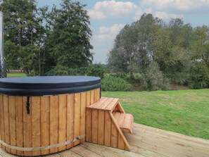 A hot tub with a wooden deck and a wooden ramp leading up to it, surrounded by greenery. - Bee Hive (Oakham)