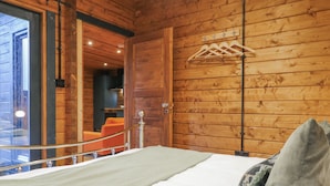 Un dormitorio de cabaña de madera con una cama, un perchero y un puerta de cristal que da a un balcón.