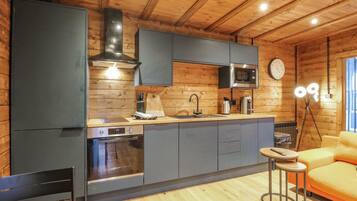 A modern kitchen with wooden walls, a built-in oven, a microwave, and a sink. There is a bar stool and a yellow sofa in the living area.