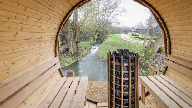 Una estructura de madera con un vano circular, un banco y vistas a un río y vegetación.