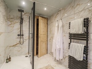 A modern bathroom with a glass-enclosed shower, marble walls, wooden door, and a towel rack with multiple towels. - Bee Hive (Oakham)