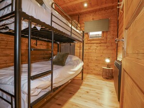 A bunk bed room with wooden walls and a small table with a lamp. - Bee Hive (Oakham)