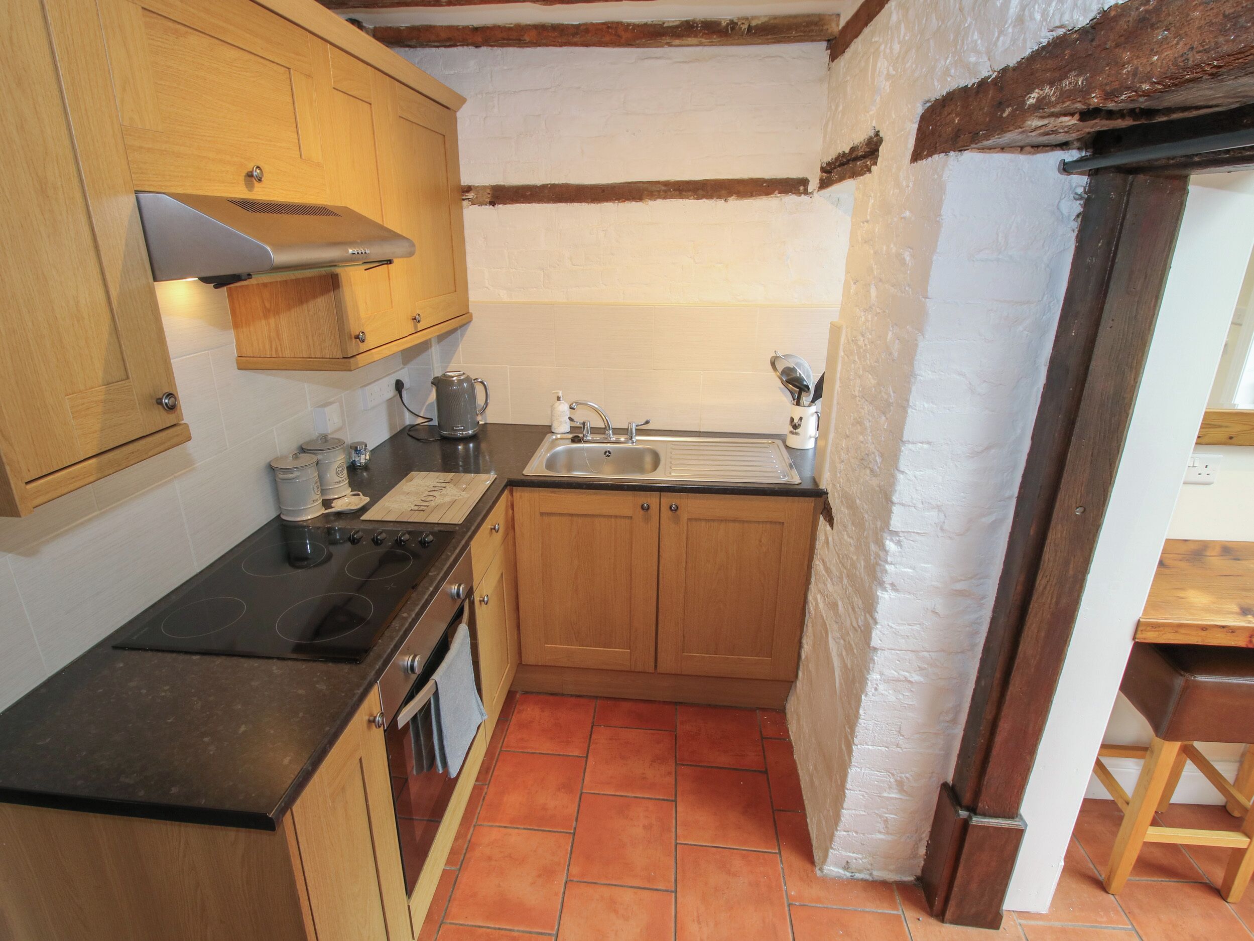 A compact kitchen with wooden cabinets, a black countertop, a stove, and a sink.