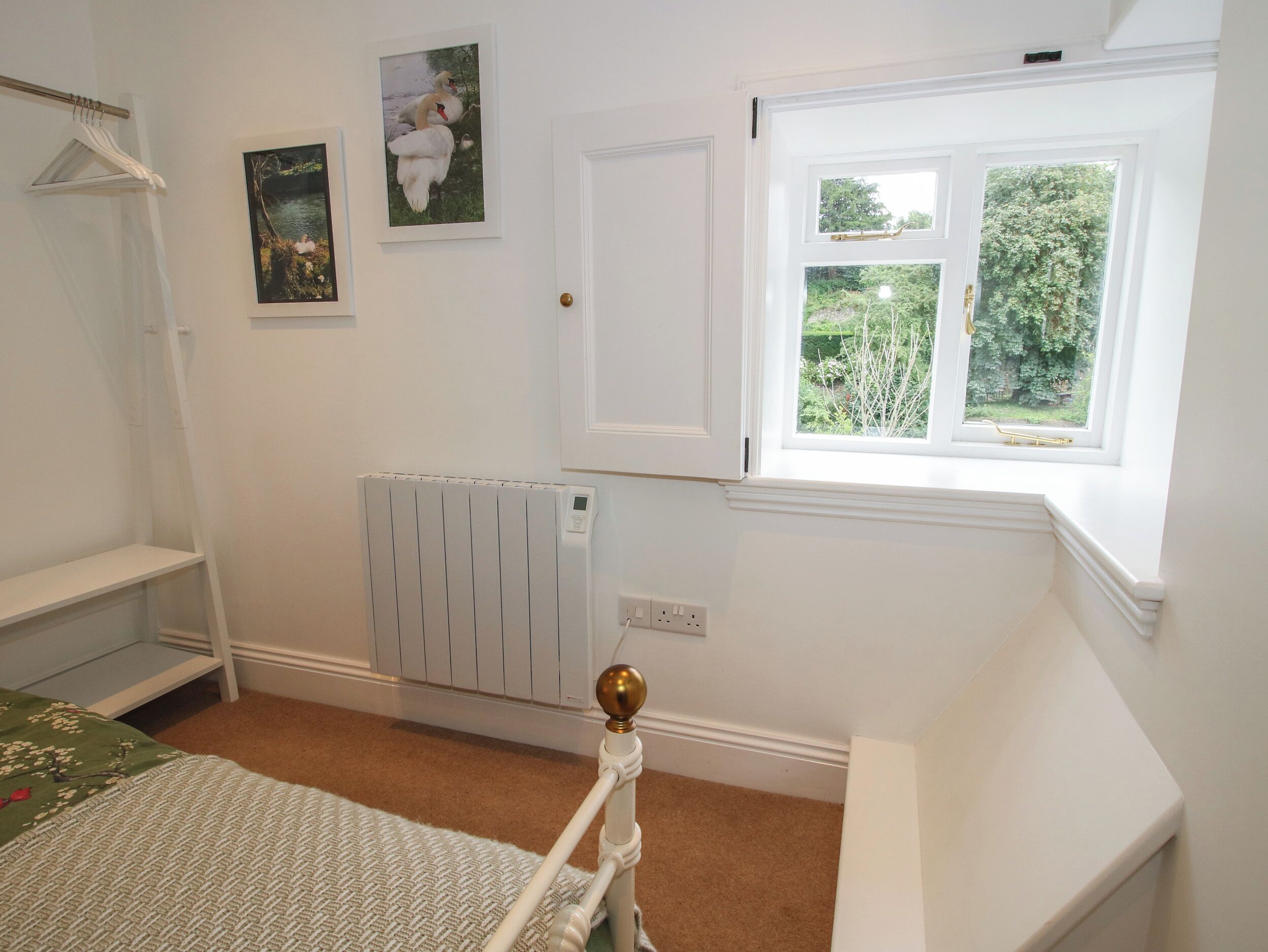 Une chambre avec un radiateur, une fenêtre donnant sur un paysage verdoyant et un lit recouvert d’une couvre-lit verte et blanche.