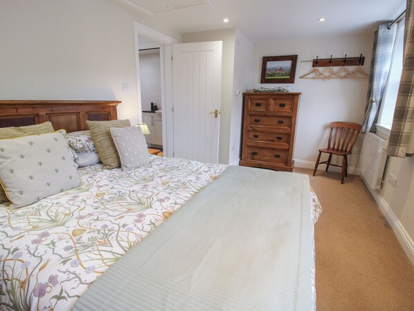 A bedroom with a bed, a dresser, a chair, and a coat rack. - Moorhen Cottage (Ludlow)